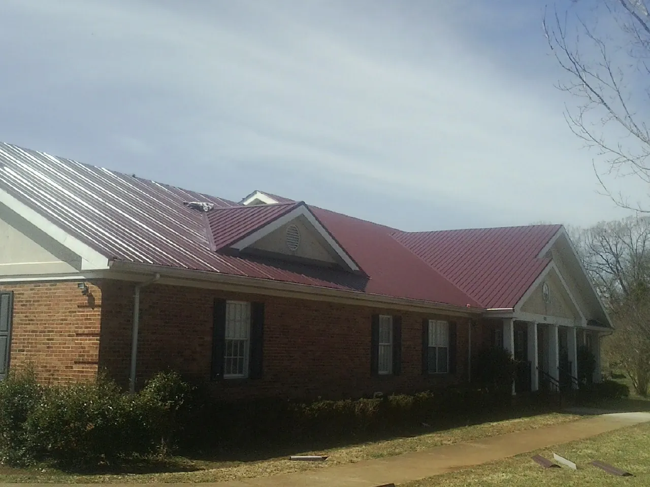 Red metal roof with gabled entries on a long brick building, from a Hail Damage Roof Repair job in Cranberry