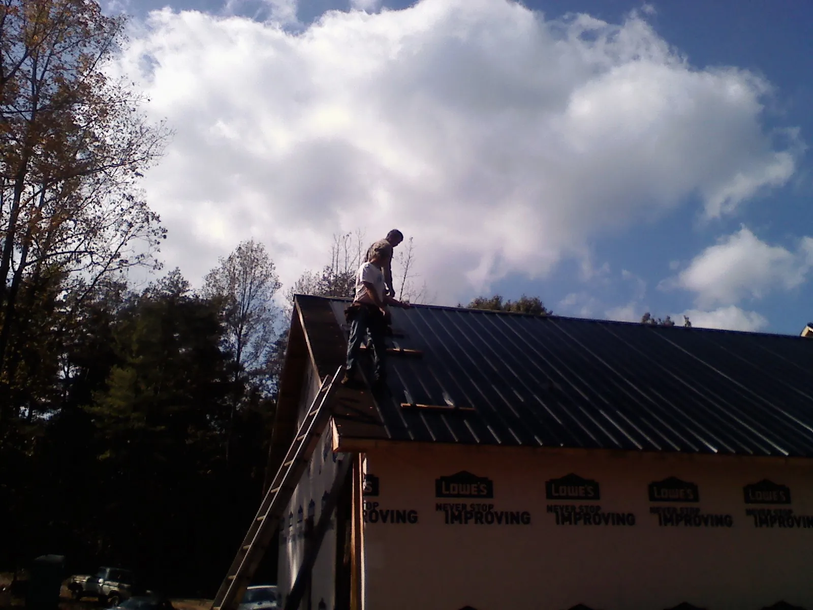 Roofer fastening dark metal panels high against a cloudy sky, from a Roof Inspection job in Cranberry
